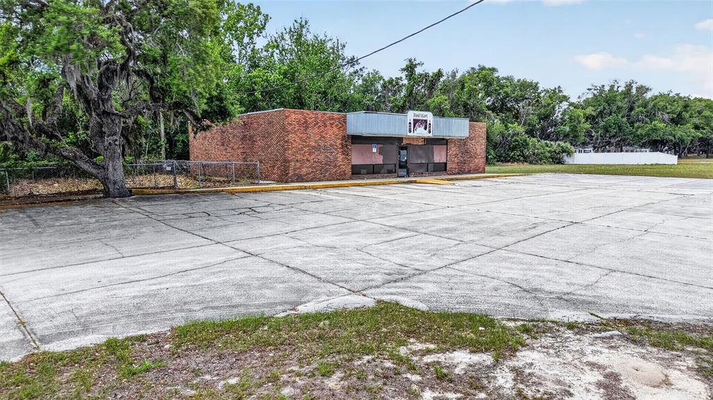 A vacant brick commercial building with a large concrete parking lot and surrounding trees — 2501 SOUTH STREET, LEESBURG, FL