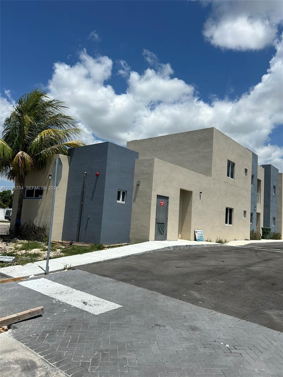 A two-story building with tan and gray stucco walls stands next to a paved parking lot — 811 E 52nd St # 102, Hialeah FL 33013, HIALEAH, FL