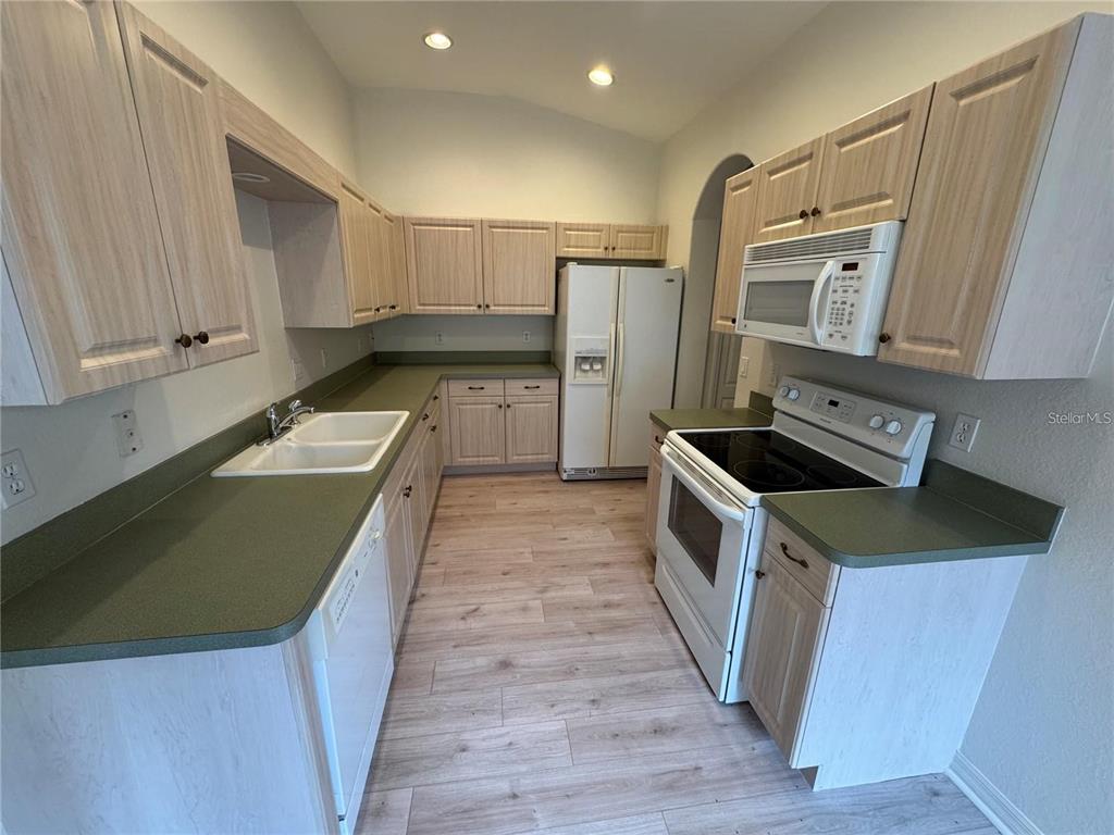 A kitchen features light wood cabinets, green countertops, white appliances, and light wood-look flooring — 315 AUBURN WOODS CIRCLE, VENICE, FL