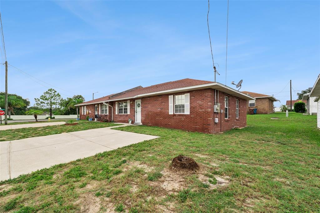 A single-story brick duplex with a concrete driveway and a grassy yard under a blue sky — 1433 THOUSAND ROSES AVENUE W, LAKE WALES, FL