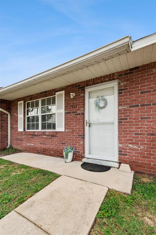 A brick exterior features a white front door, a window with shutters, and a concrete walkway — 1433 THOUSAND ROSES AVENUE W, LAKE WALES, FL