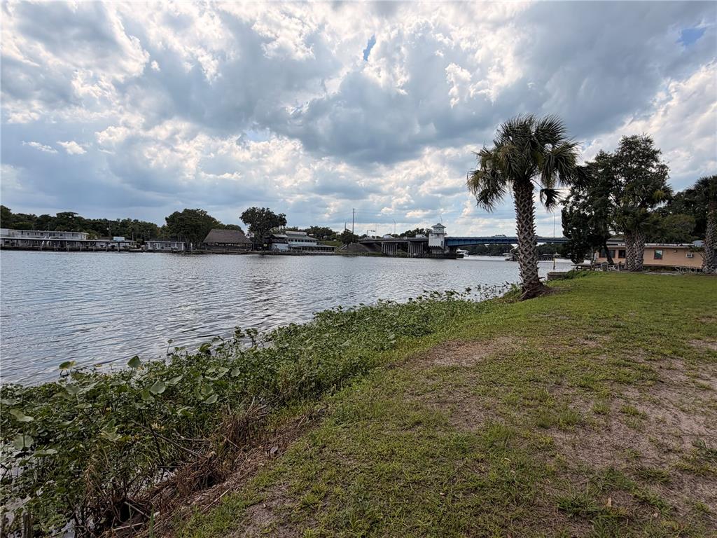 A grassy waterfront lawn overlooks a river with a bridge and buildings in the distance — 1570 RIVEREDGE COURT, ASTOR, FL