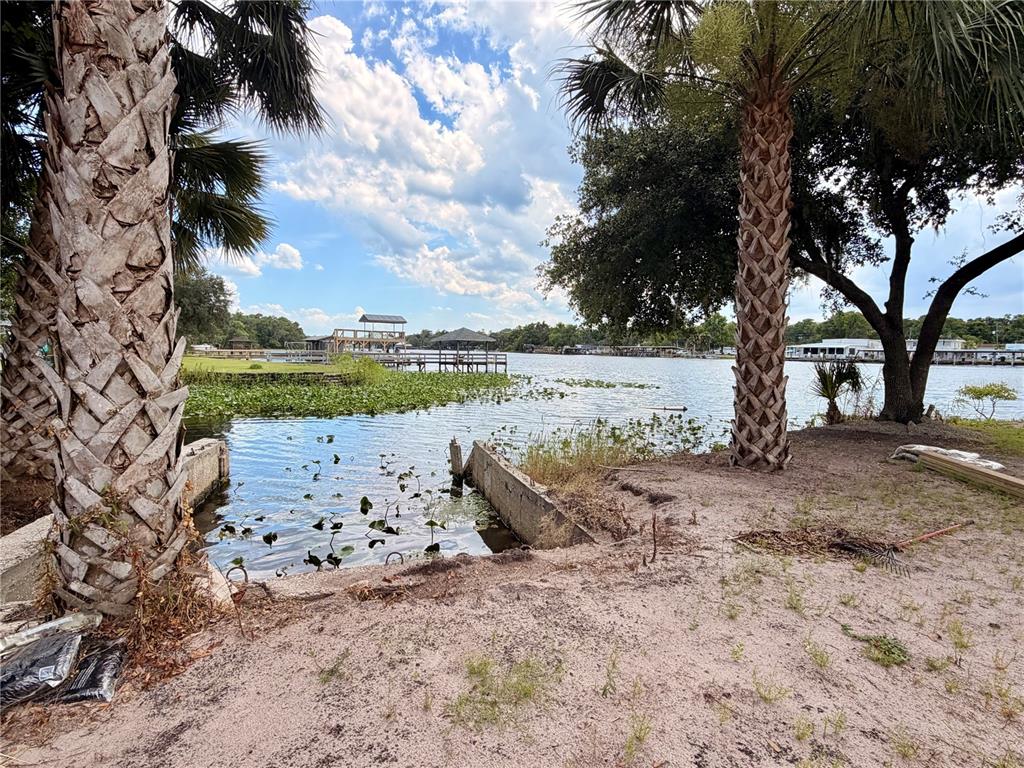 A sandy waterfront area features two palm trees framing a small concrete boat slip — 1570 RIVEREDGE COURT, ASTOR, FL