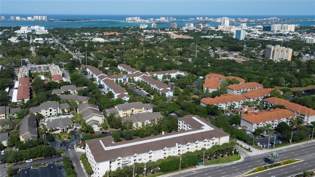 An aerial view shows a large apartment complex with multiple buildings surrounded by trees and roads — 1216 S MISSOURI AVENUE UNIT 322, CLEARWATER, FL