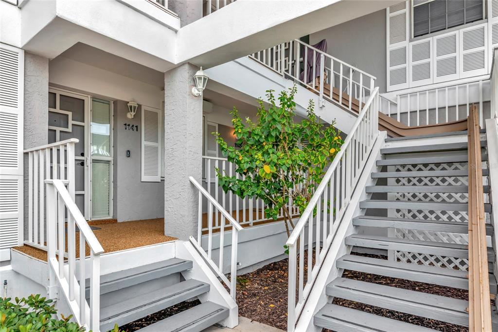 An exterior view of a multi-level building with white railings, gray stairs, and a small tree — 1145 EDGEWATER CIRCLE UNIT 1145, BRADENTON, FL