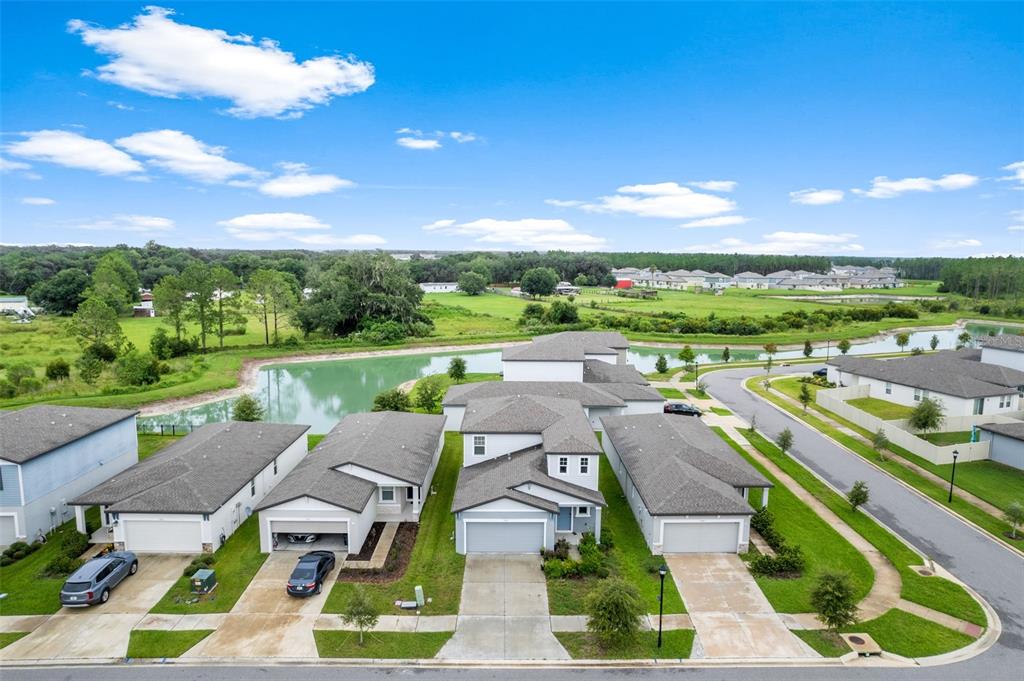 An aerial view shows several suburban houses with gray roofs and driveways near a pond — 3361 FRESNO PLACE, ZEPHYRHILLS, FL