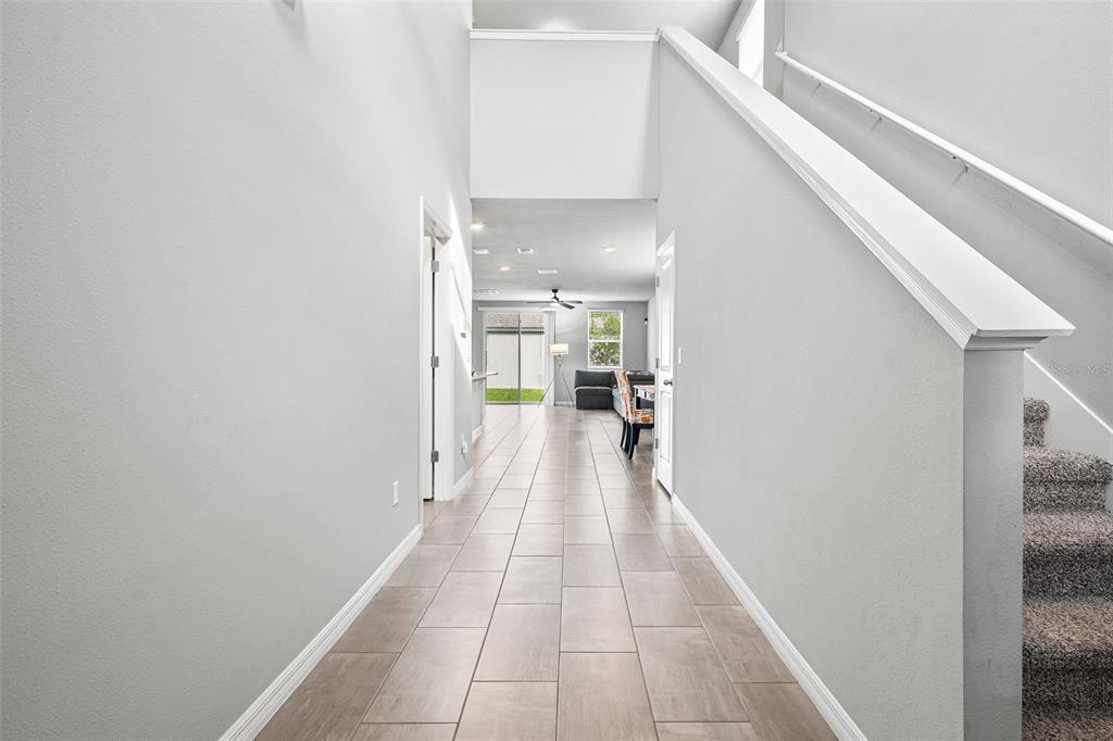 A tiled hallway leads past a staircase toward an open living area with sliding doors — 3361 FRESNO PLACE, ZEPHYRHILLS, FL