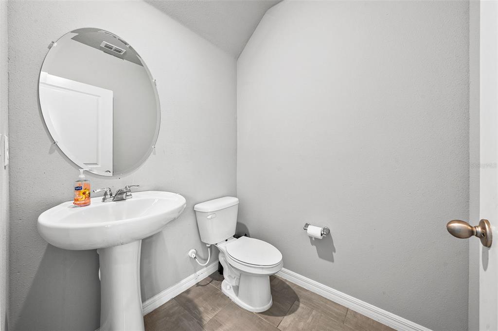 A small powder room featuring a pedestal sink, a round mirror, and a white toilet — 3361 FRESNO PLACE, ZEPHYRHILLS, FL