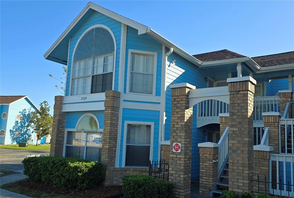 A two-story blue building features brick pillars, arched windows, and a staircase leading to balconies — 2729 N POINCIANA BOULEVARD UNIT 117, KISSIMMEE, FL