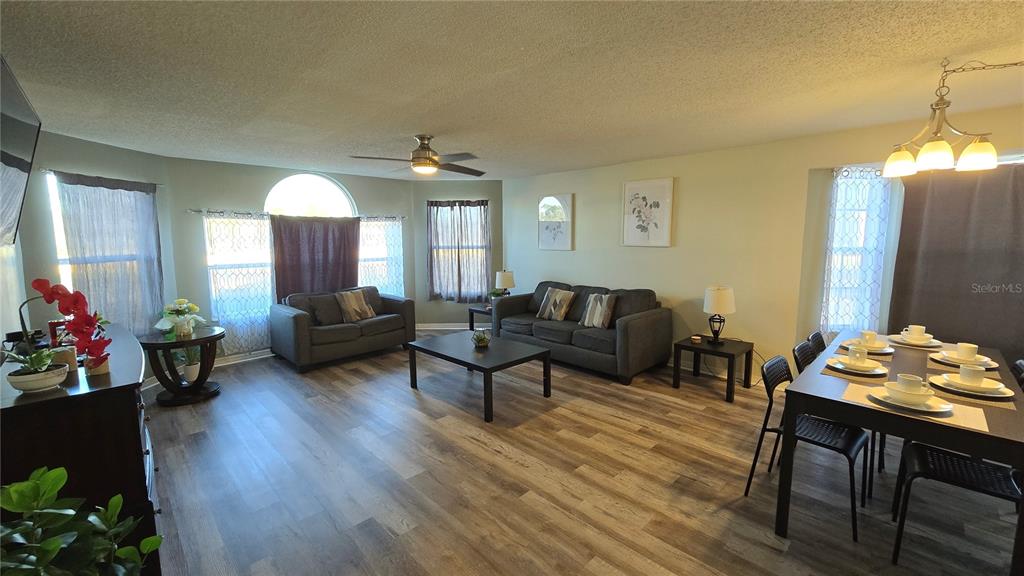 A living and dining area features wood-look flooring, gray sofas, and a dining table — 2729 N POINCIANA BOULEVARD UNIT 117, KISSIMMEE, FL