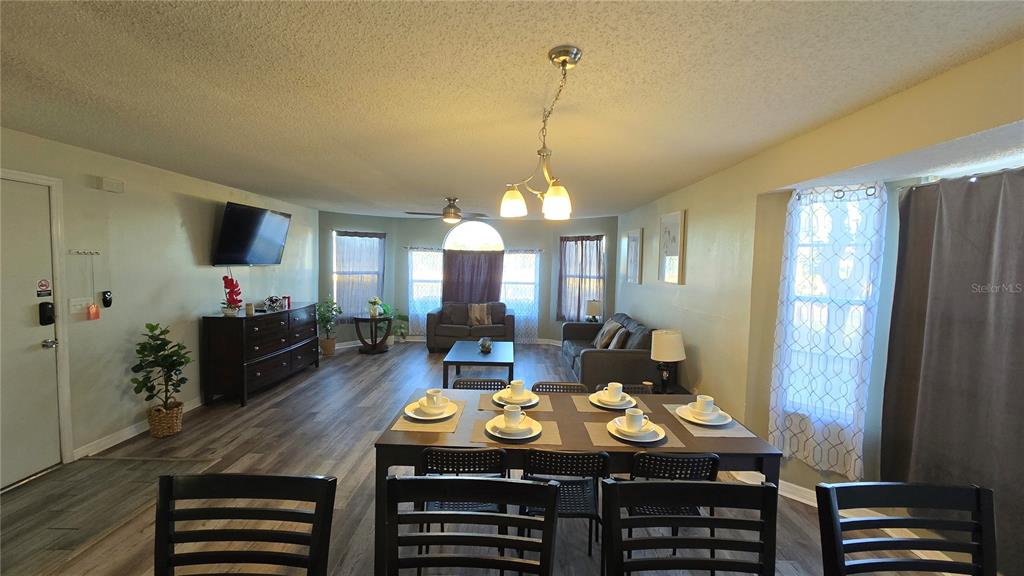 An open-concept living and dining area features wood-look flooring, a dark dining set, and neutral walls — 2729 N POINCIANA BOULEVARD UNIT 117, KISSIMMEE, FL