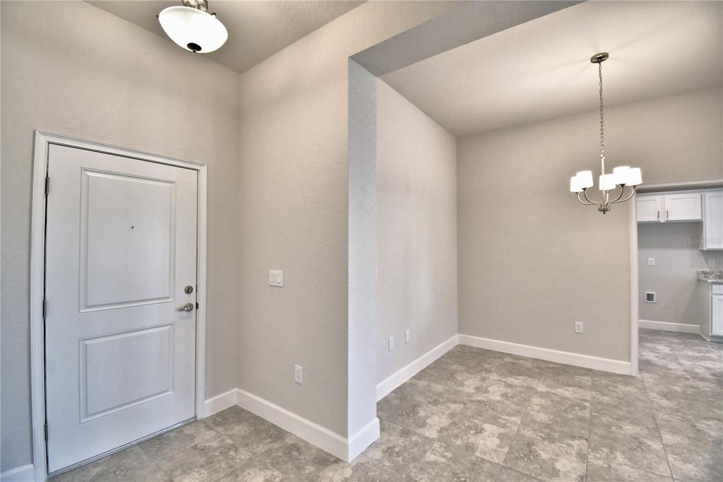 An entryway with light gray tile flooring leads into a dining area with a chandelier — 4608 CALAMINT LANE, AUBURNDALE, FL