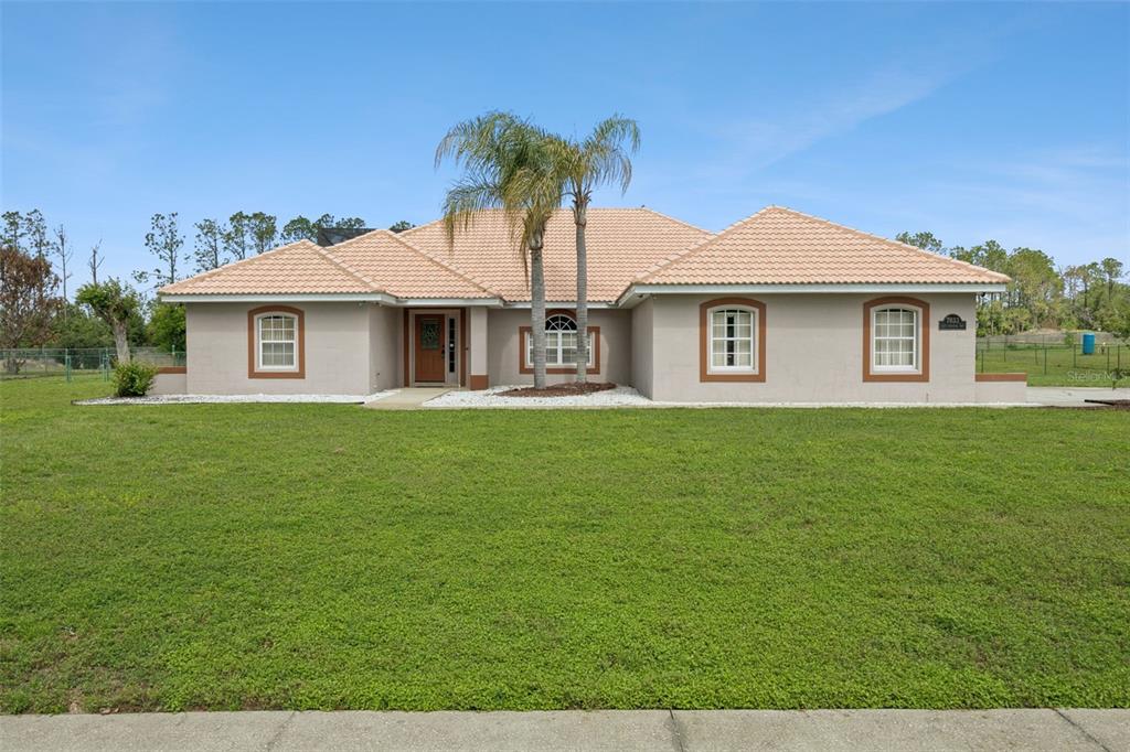 A single-story house with a beige stucco exterior, a tiled roof, and a front lawn — 7833 GOLF PARADISE WAY, CLERMONT, FL