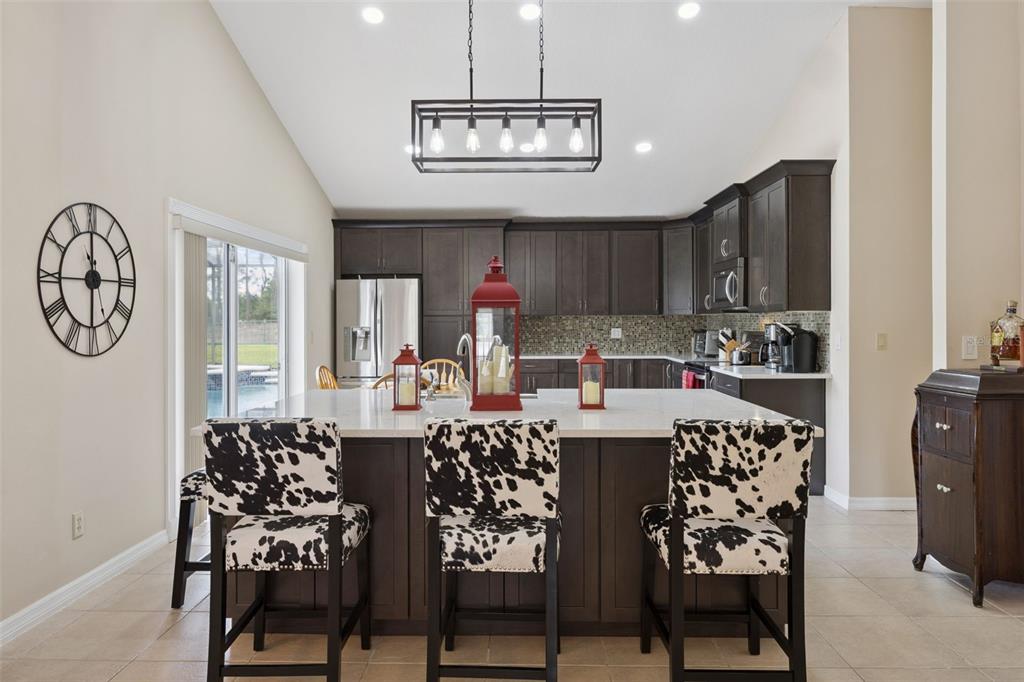 A kitchen features dark wood cabinets, a white island with cow-print stools, and pendant lighting — 7833 GOLF PARADISE WAY, CLERMONT, FL