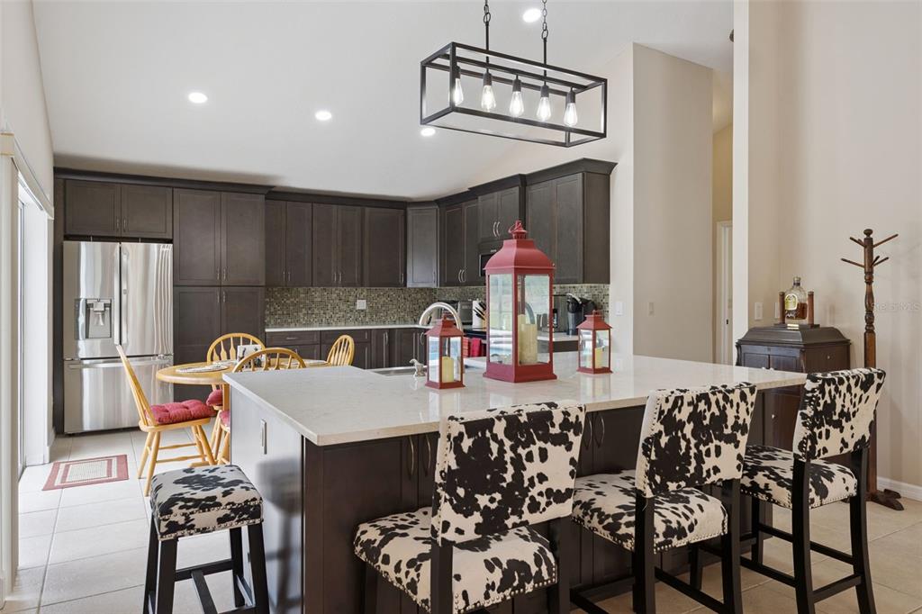 A kitchen features dark wood cabinets, a white quartz island, and cow-print bar stools — 7833 GOLF PARADISE WAY, CLERMONT, FL