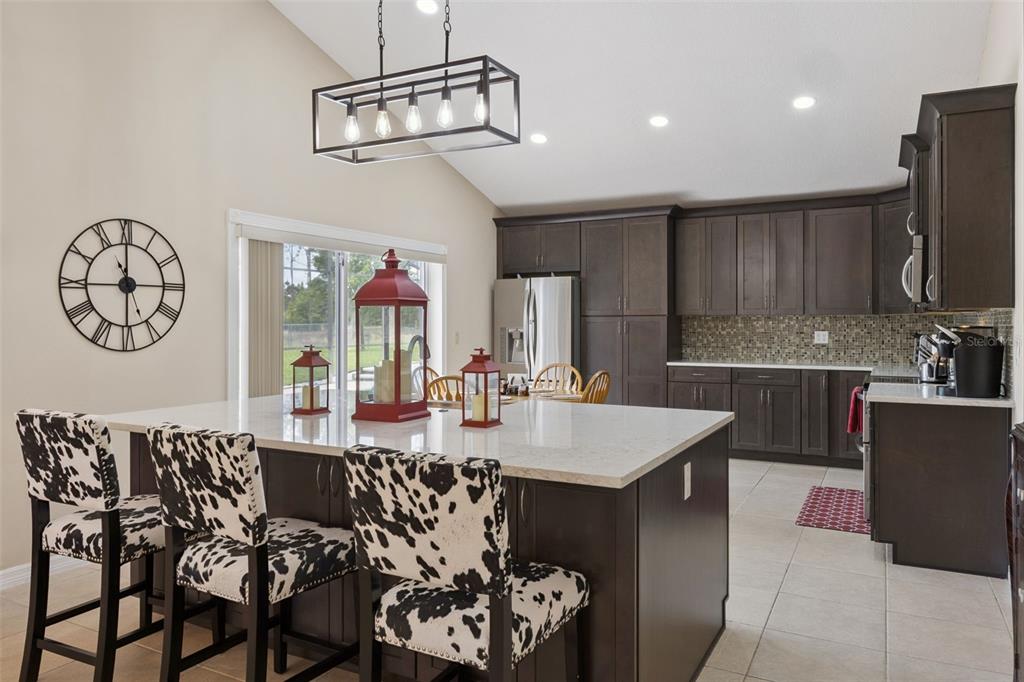 A kitchen features dark wood cabinets, a large island with cow-print stools, and vaulted ceilings — 7833 GOLF PARADISE WAY, CLERMONT, FL