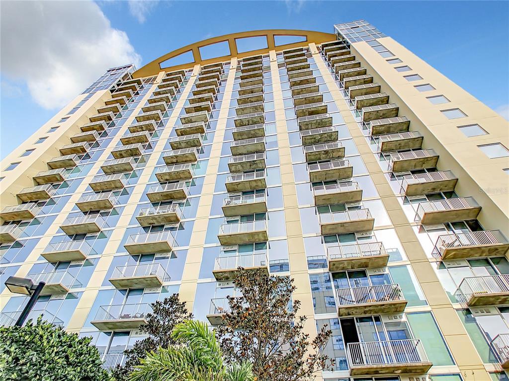 A low-angle view of a tall, modern high-rise building with numerous balconies and glass windows — 155 S COURT AVENUE UNIT 2107, ORLANDO, FL