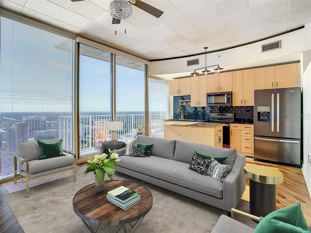 A modern living room and kitchen area with floor-to-ceiling windows overlooking a city skyline — 155 S COURT AVENUE UNIT 2107, ORLANDO, FL