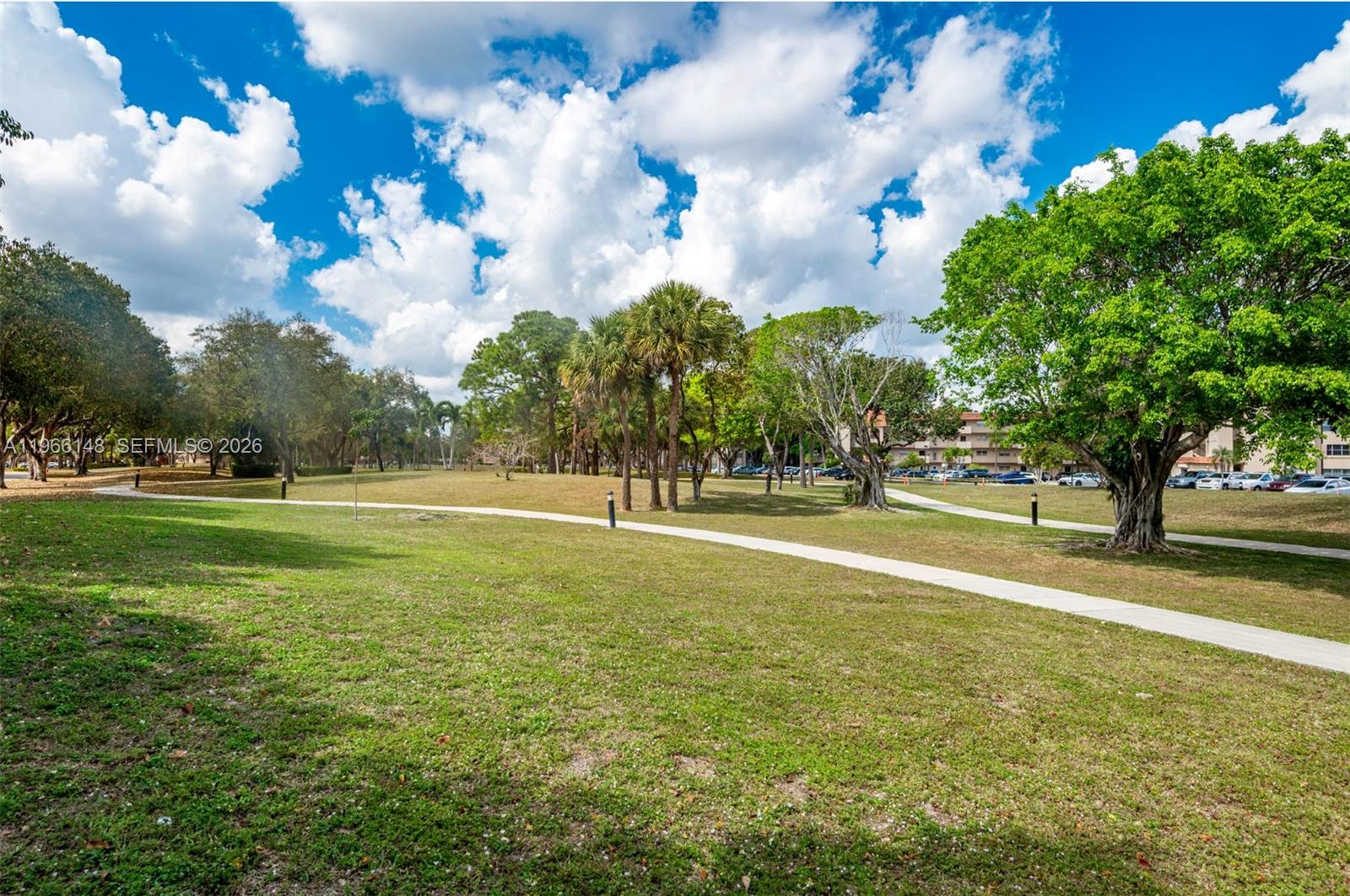 A paved walking path winds through a grassy park area with scattered trees and palm trees — 6301 N Fall Circle Dr # 213, Lauderhill FL 33319, LAUDERHILL, FL