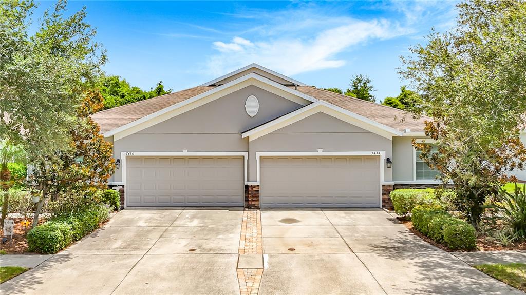 A duplex house features two garage doors, a concrete driveway, and surrounding landscaping — 7434 SURREY PINES DRIVE, APOLLO BEACH, FL