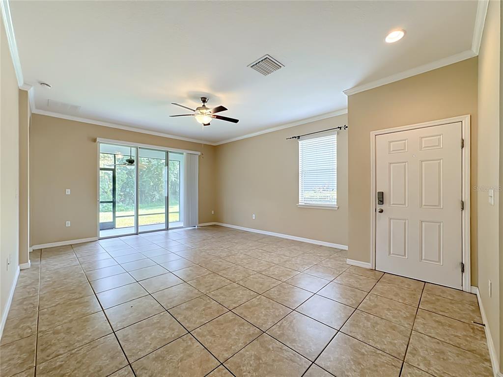 An empty living room features beige walls, tile flooring, a ceiling fan, and a sliding door — 7434 SURREY PINES DRIVE, APOLLO BEACH, FL