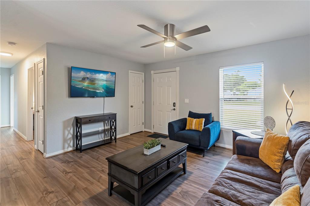 A living room features wood-look flooring, a ceiling fan, a wall-mounted television, and a sofa — 6600 NW 62ND PLACE, OCALA, FL