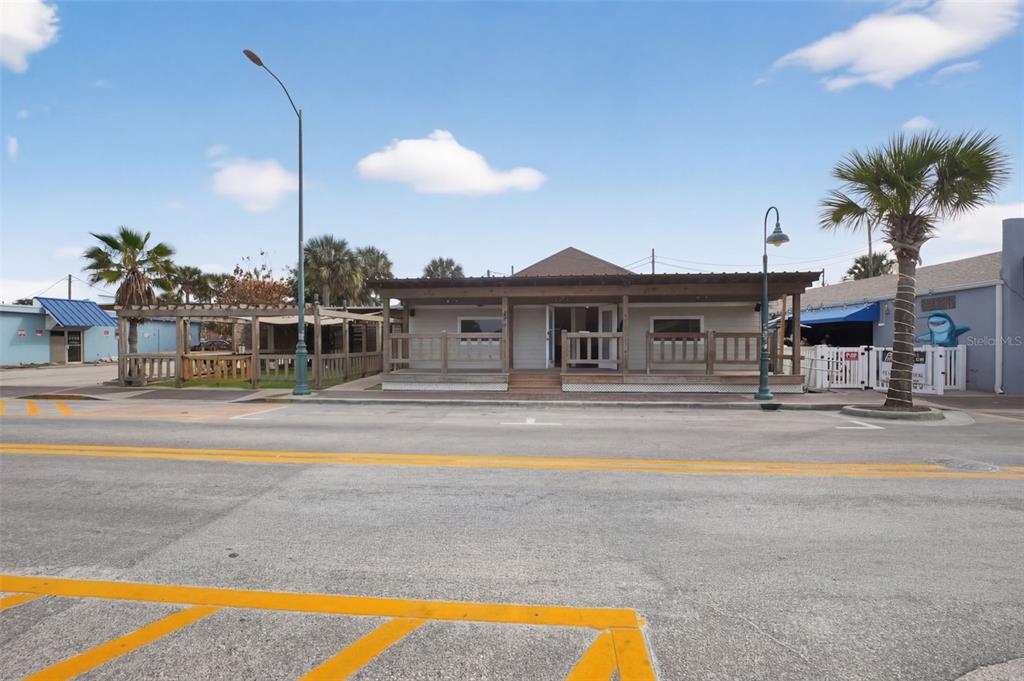 A single-story commercial building with a wooden porch sits along a street with palm trees — 411 FLAGLER AVENUE UNIT B, NEW SMYRNA BEACH, FL
