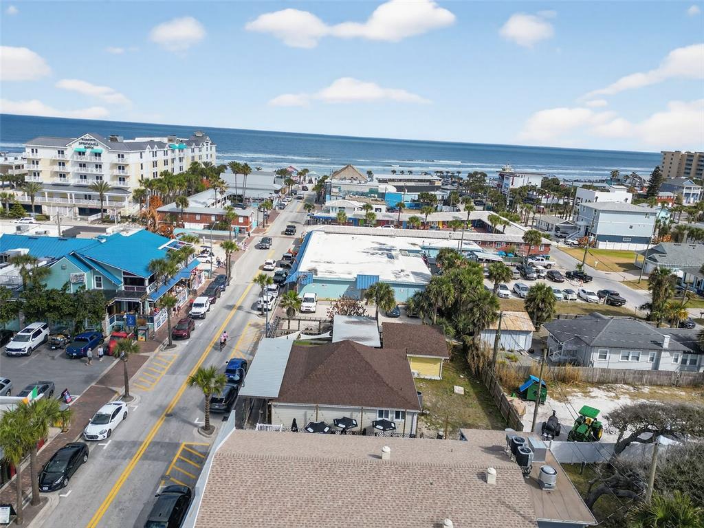 An aerial view shows a coastal street with buildings, parked cars, and the ocean beyond — 411 FLAGLER AVENUE UNIT B, NEW SMYRNA BEACH, FL