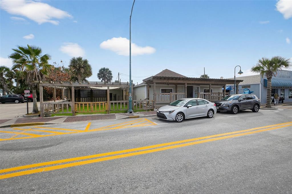 An exterior view of a commercial building with a wooden porch and adjacent outdoor seating area — 411 FLAGLER AVENUE UNIT B, NEW SMYRNA BEACH, FL