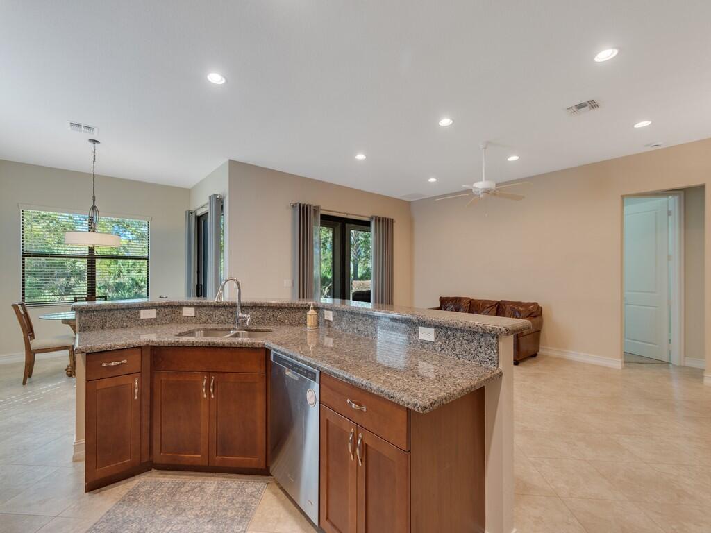 A kitchen with granite countertops, wood cabinets, and a stainless steel dishwasher overlooks a living area — 4338 56th Lane, Vero Beach FL 32967, VERO BEACH, FL