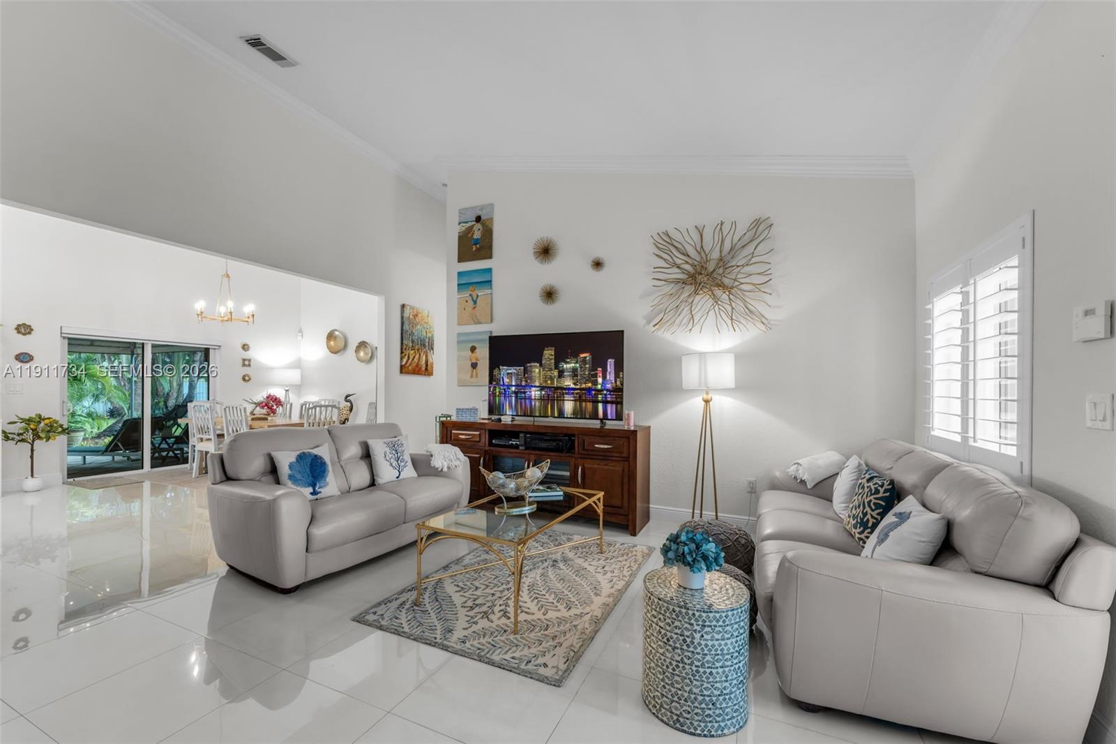 A bright living room features light-colored leather sofas, a glass coffee table, and tile flooring — 12743 SW 220th St, Miami FL 33170, MIAMI, FL
