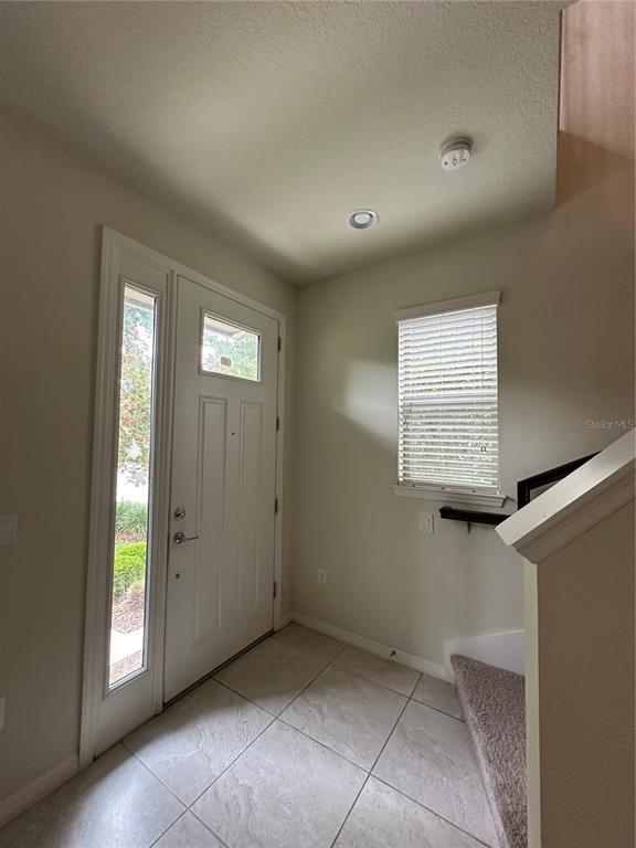 An entryway features tiled flooring, a front door with a sidelight, and a carpeted staircase — 527 PIAZZA POINT, OVIEDO, FL