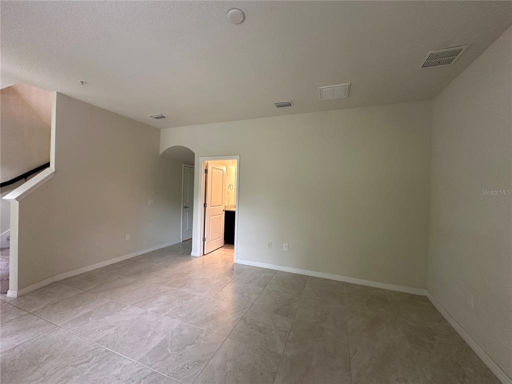An empty room with light-colored tile flooring, beige walls, and a doorway leading to a bathroom — 527 PIAZZA POINT, OVIEDO, FL