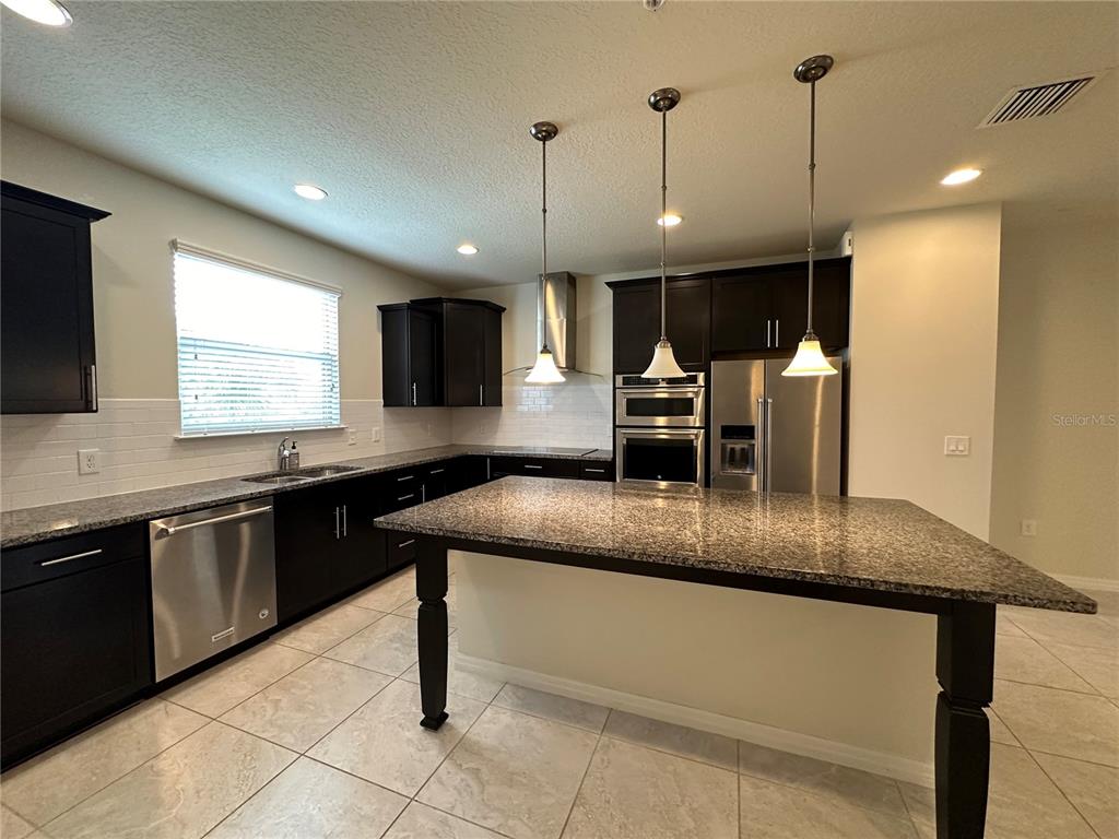 A kitchen features dark cabinetry, granite countertops, stainless steel appliances, and a large center island — 527 PIAZZA POINT, OVIEDO, FL