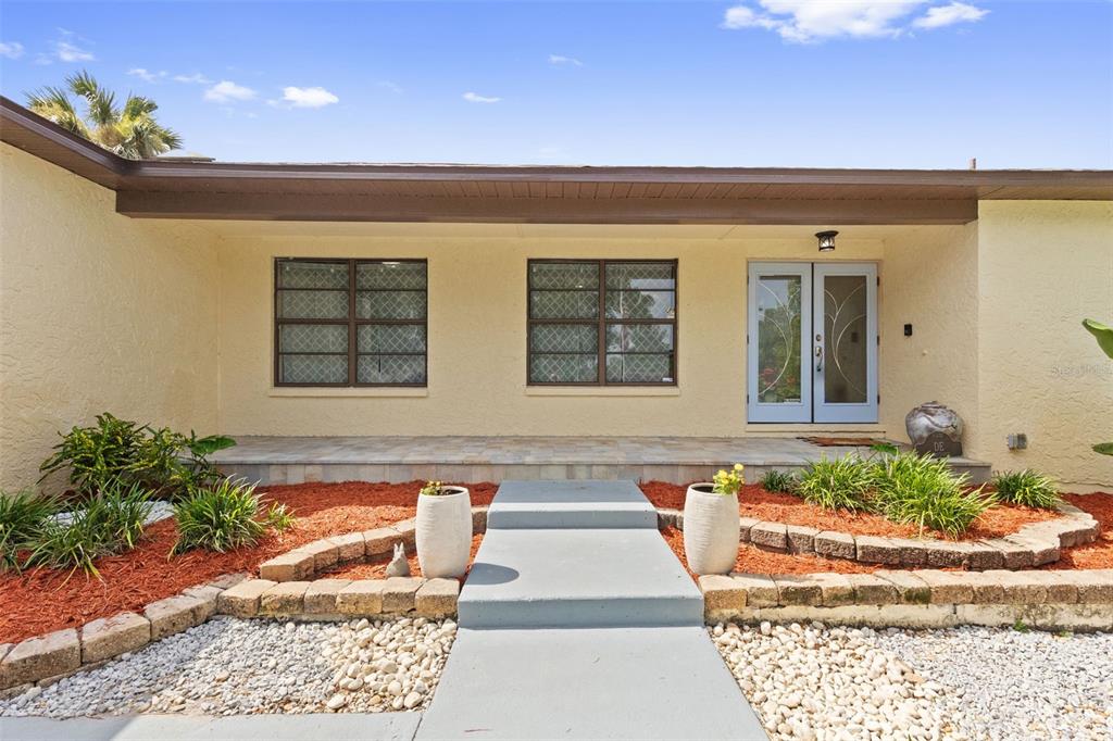 A single-story house exterior features a covered porch, two windows, and a light blue door — 2311 LONG GREEN COURT, VALRICO, FL
