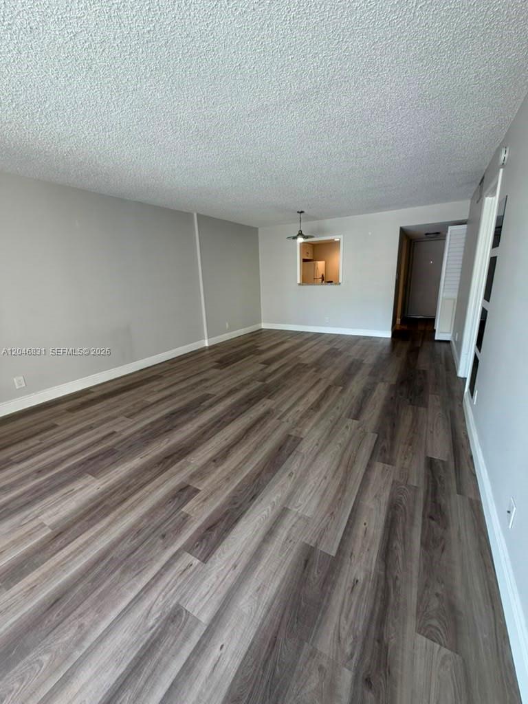 An empty living room features gray walls, wood-look flooring, and a pass-through window to the kitchen — 408 NW 68th Ave # 209, Plantation FL 33317, PLANTATION, FL