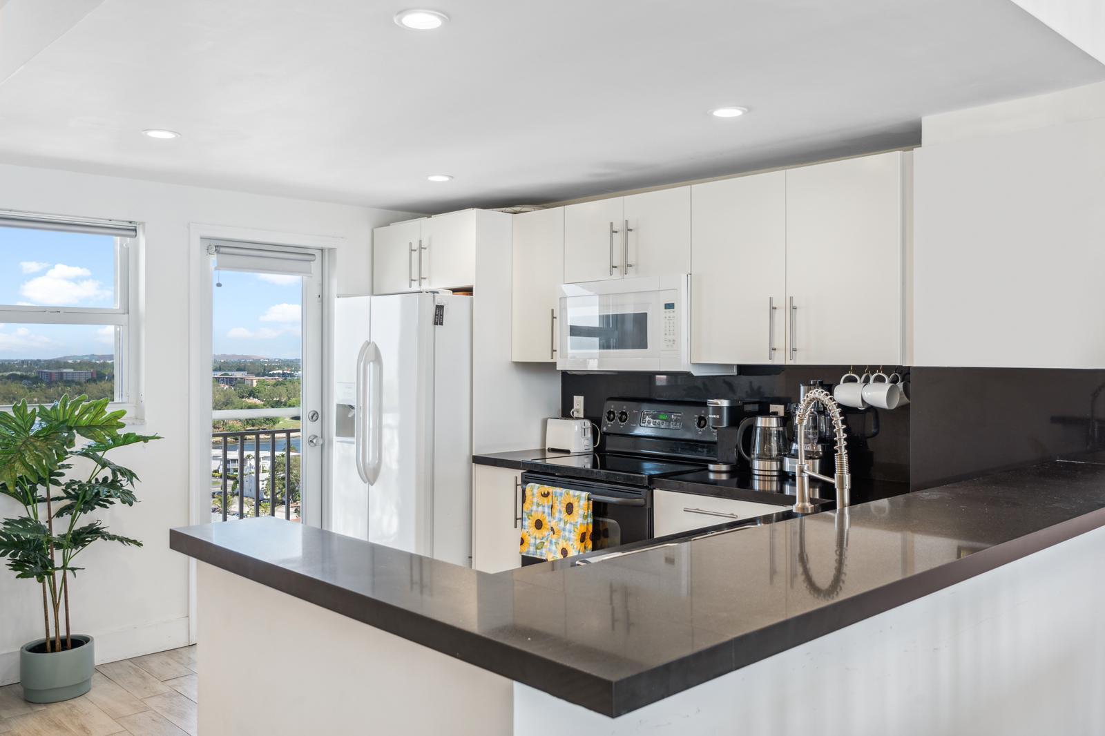 A kitchen with white cabinets, black countertops, stainless steel appliances, and a balcony door view — 750 N Ocean Boulevard # 1507, Pompano Beach FL 33062, POMPANO BEACH, FL