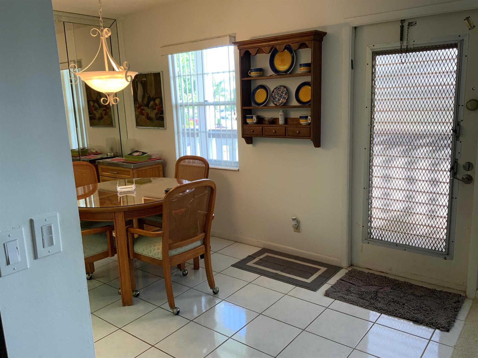 A dining area features a glass-topped table, cane-back chairs, a wall-mounted shelf, and tiled floors — 2050 Hythe C, Boca Raton FL 33434, BOCA RATON, FL
