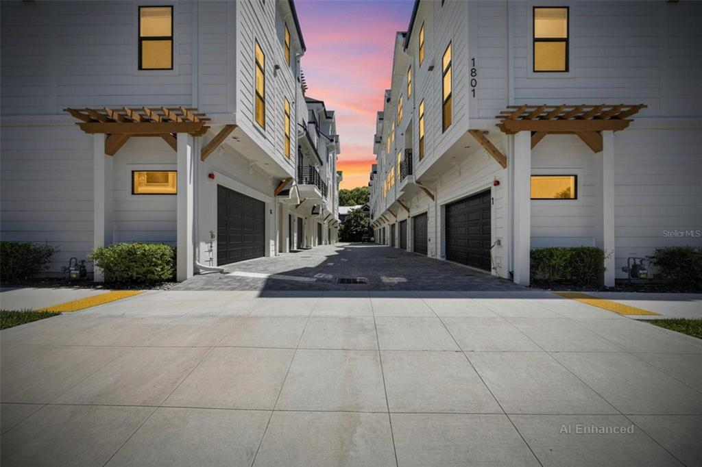 A paved driveway leads between two modern white townhomes with dark garage doors and pergolas — 1801 N MORGAN STREET UNIT 11, TAMPA, FL