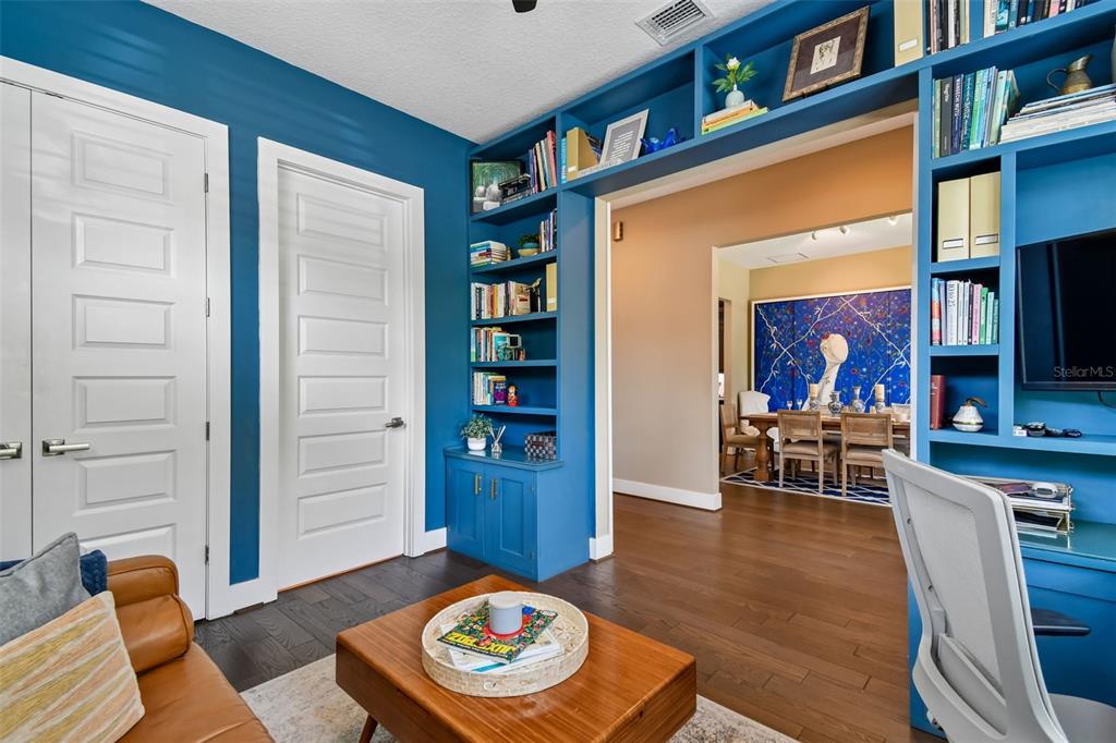 A home office features blue built-in bookshelves, a wooden coffee table, and a view into a dining room — 2107 HARGILL DRIVE, ORLANDO, FL
