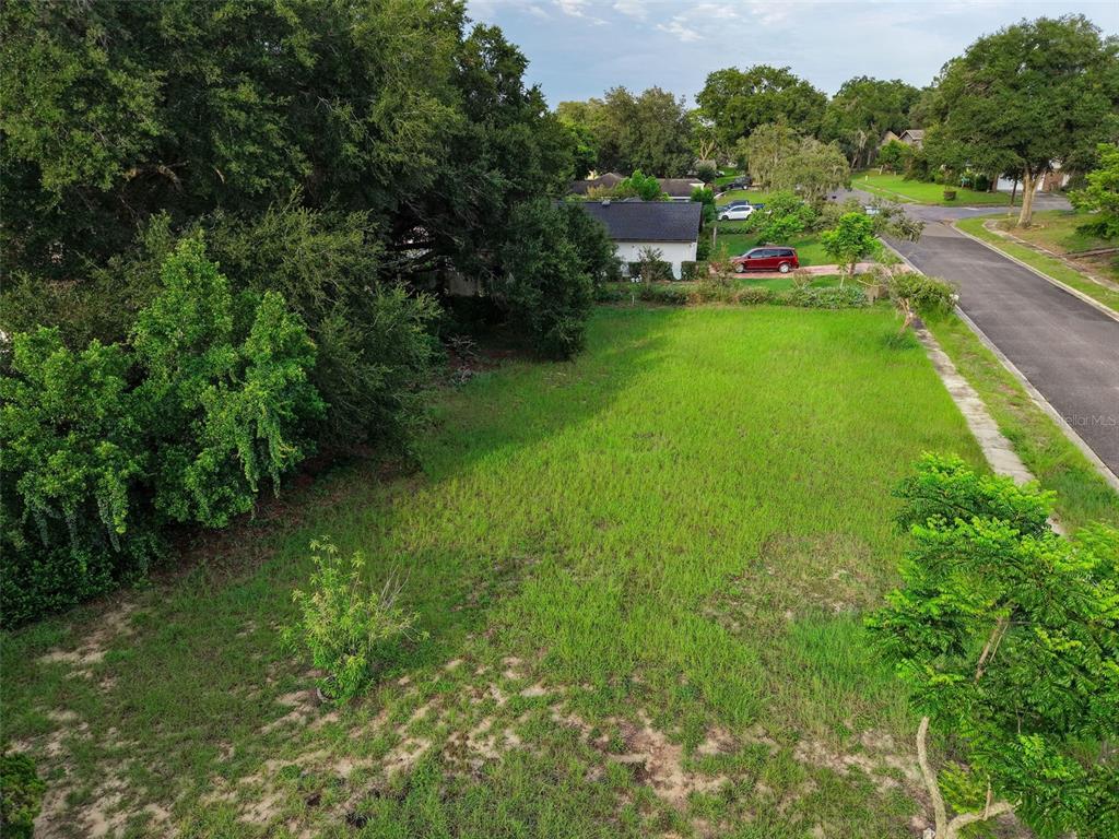 An aerial view shows a vacant, grassy residential lot bordered by trees and a paved road — SAIL FISH AVENUE, FRUITLAND PARK, FL