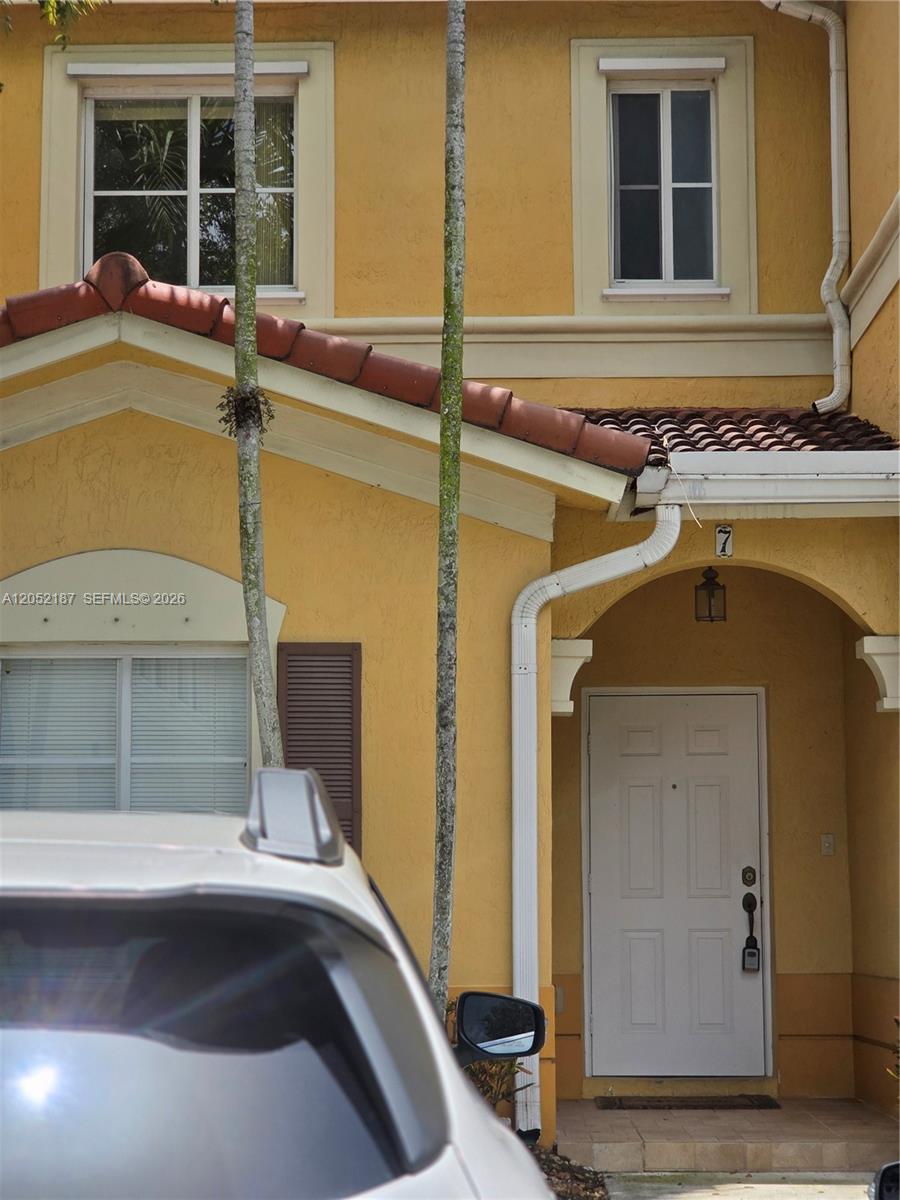 The exterior of a yellow two-story townhouse features a white front door and palm trees — DORAL, FL