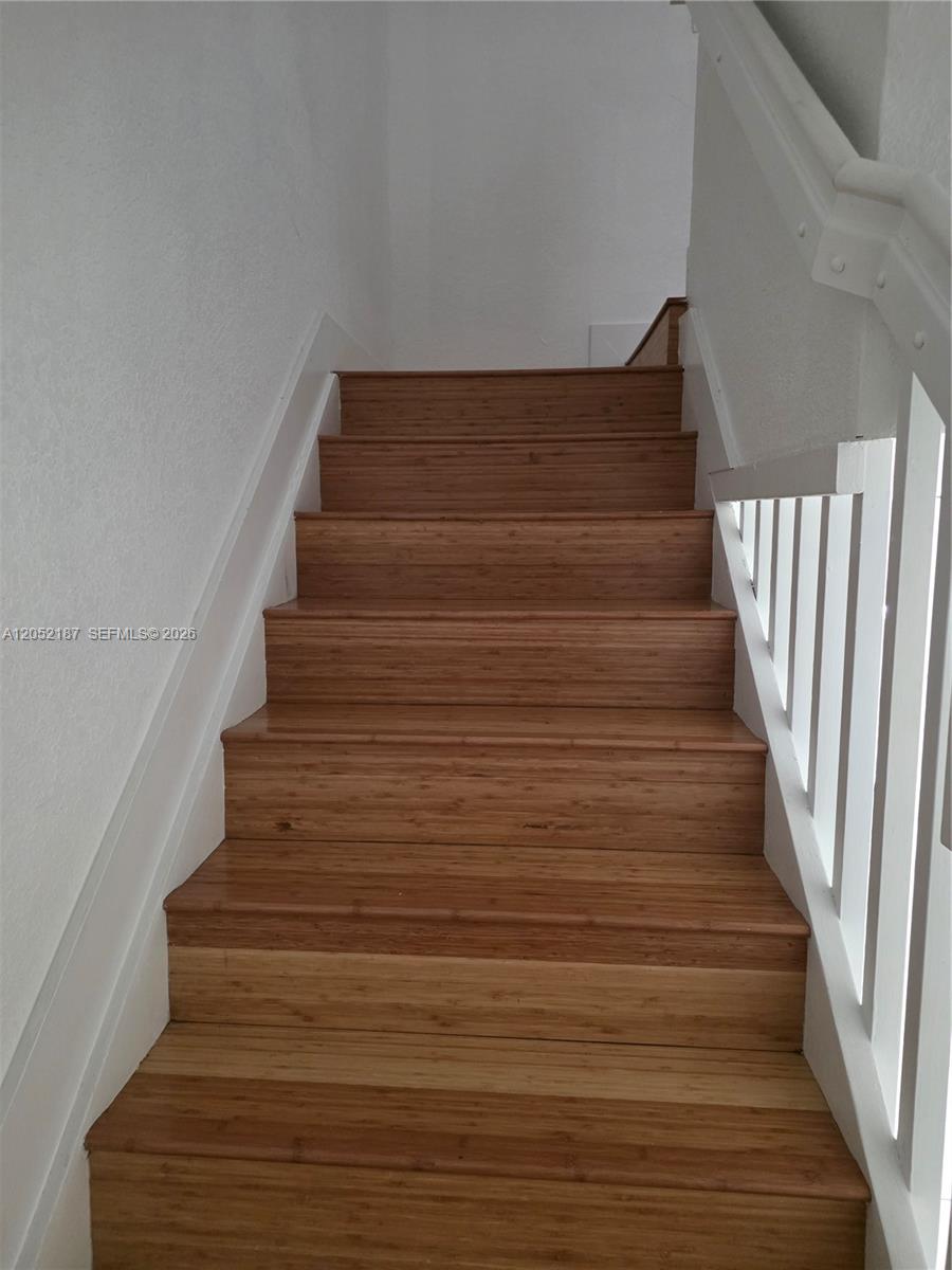 A staircase features wooden steps, white walls, and a white wooden handrail — DORAL, FL