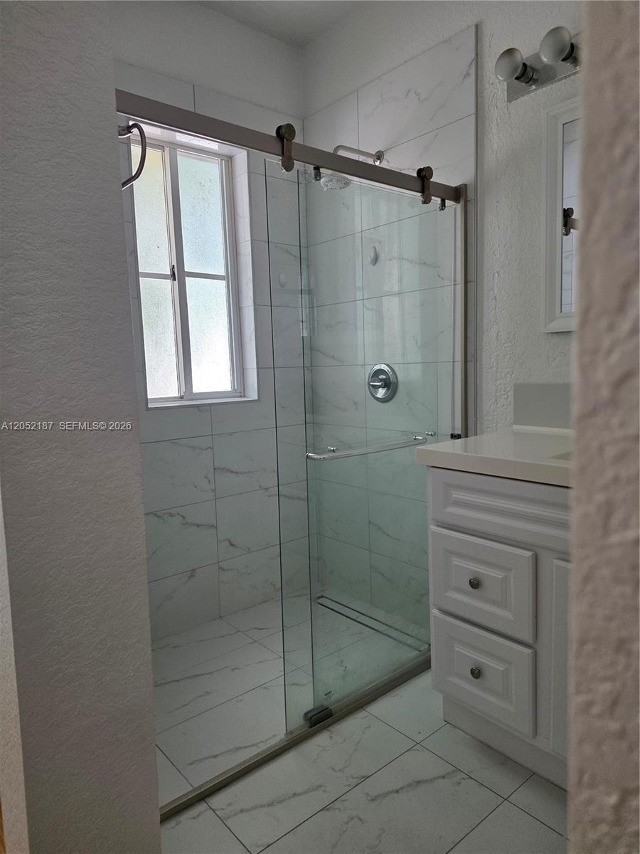 A bathroom features a glass-enclosed walk-in shower with white marble-patterned tile and a vanity — DORAL, FL