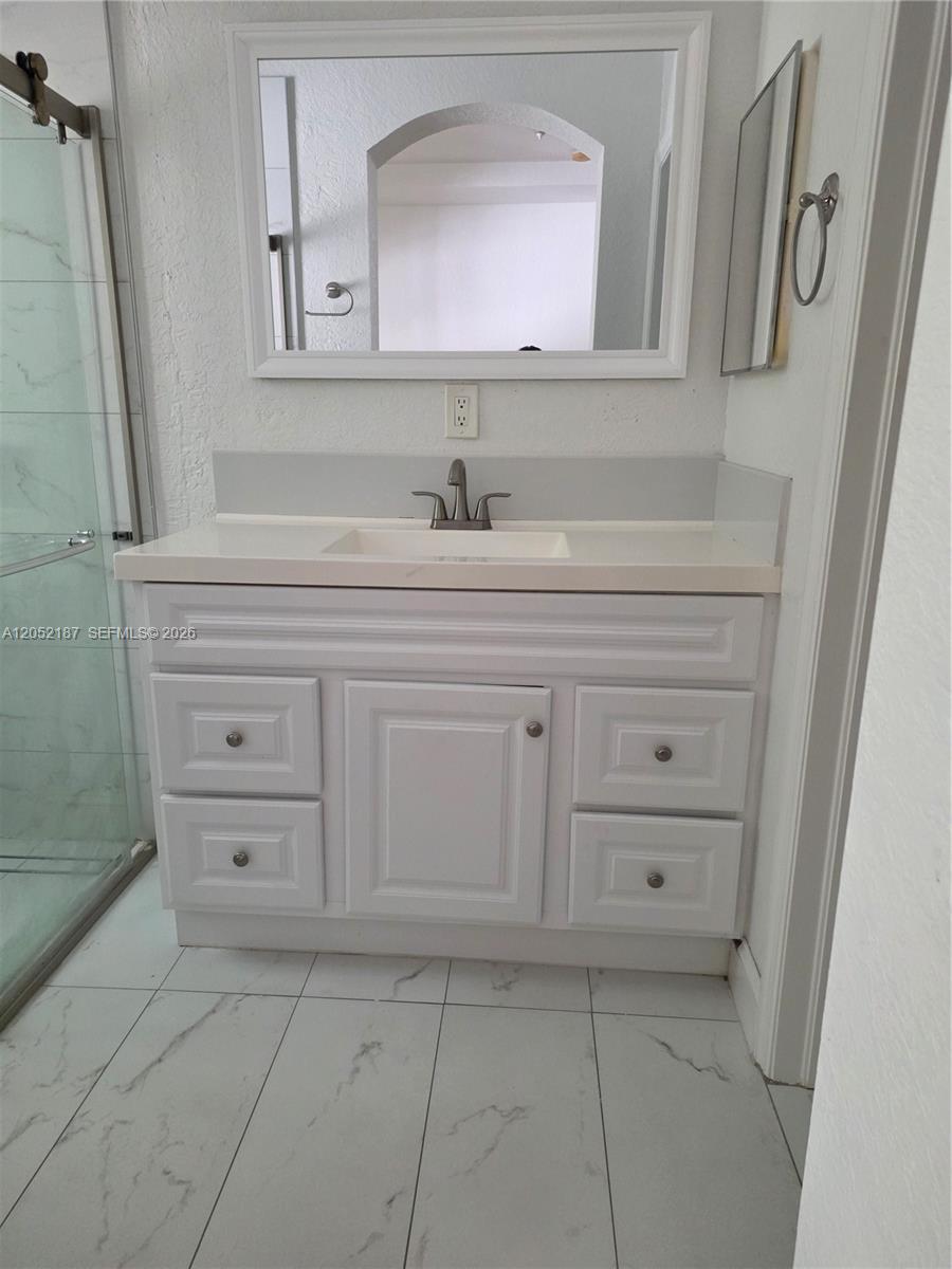 A white bathroom vanity with a sink, mirror, and tiled floor is shown — DORAL, FL