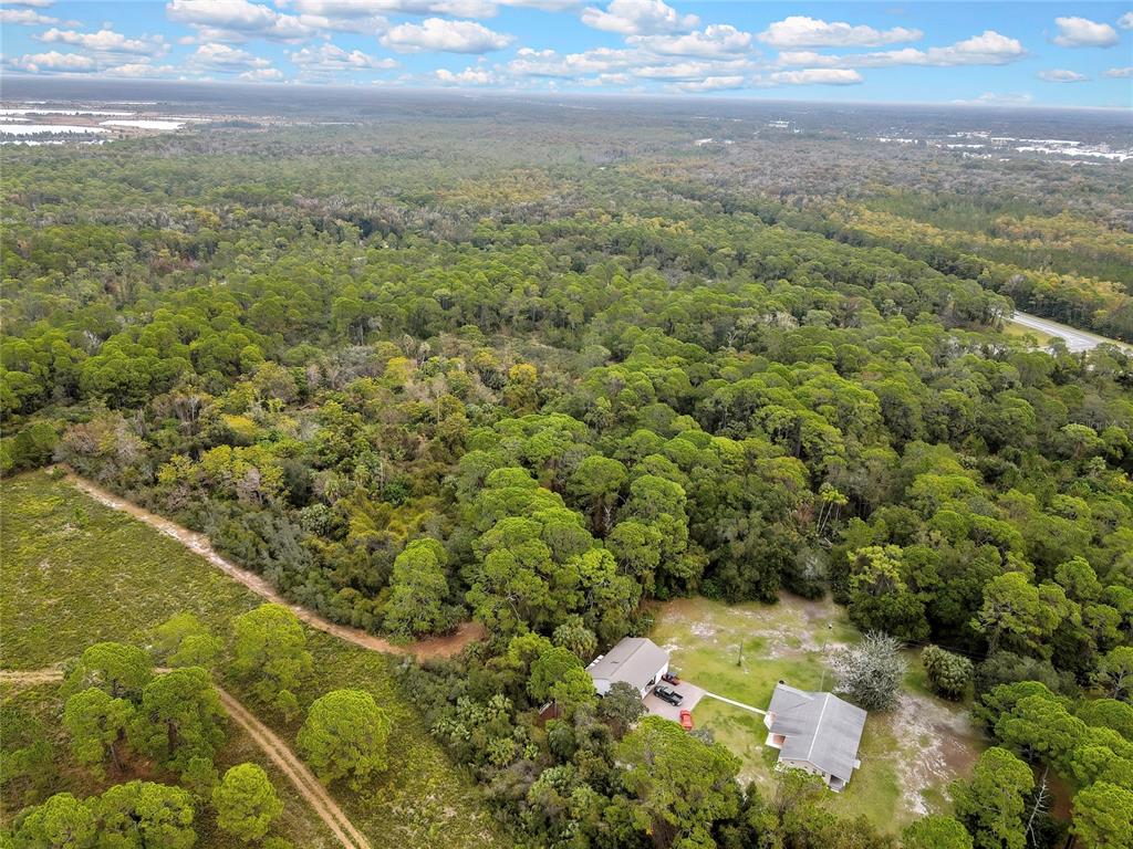 An aerial view shows two houses surrounded by dense forest and a dirt access road — SHOAL LINE BOULEVARD, SPRING HILL, FL