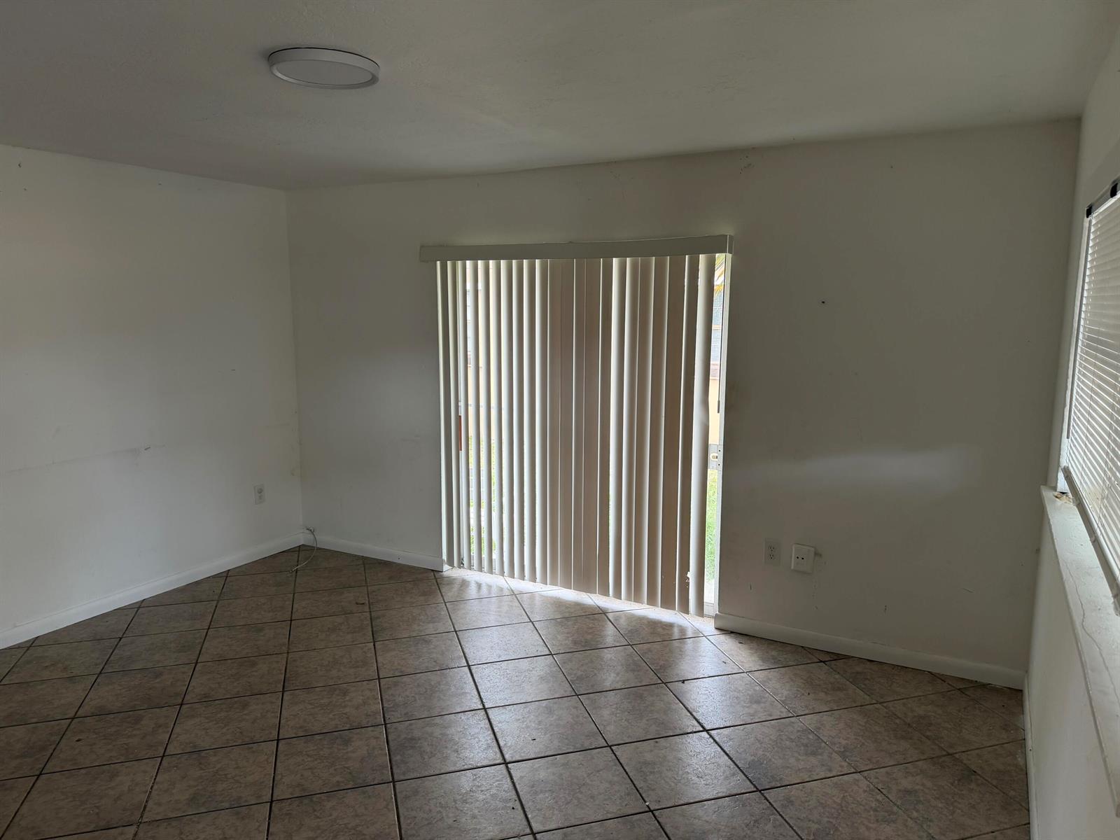 An empty room with tile flooring, white walls, vertical blinds, and a sliding glass door — 115 Maple Avenue, Fort Pierce FL 34982, FORT PIERCE, FL