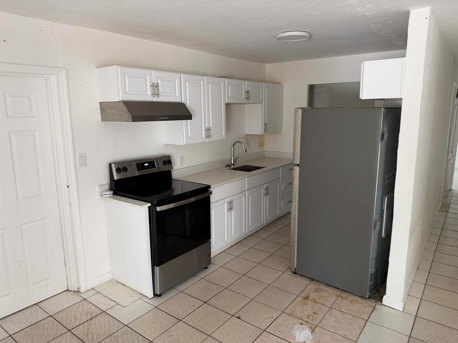 A kitchen features white cabinets, stainless steel appliances, a sink, and light-colored tile flooring — 115 Maple Avenue, Fort Pierce FL 34982, FORT PIERCE, FL
