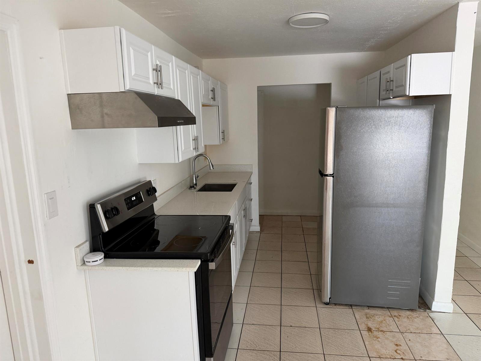A kitchen features white cabinets, stainless steel appliances, a tiled floor, and a sink — 115 Maple Avenue, Fort Pierce FL 34982, FORT PIERCE, FL
