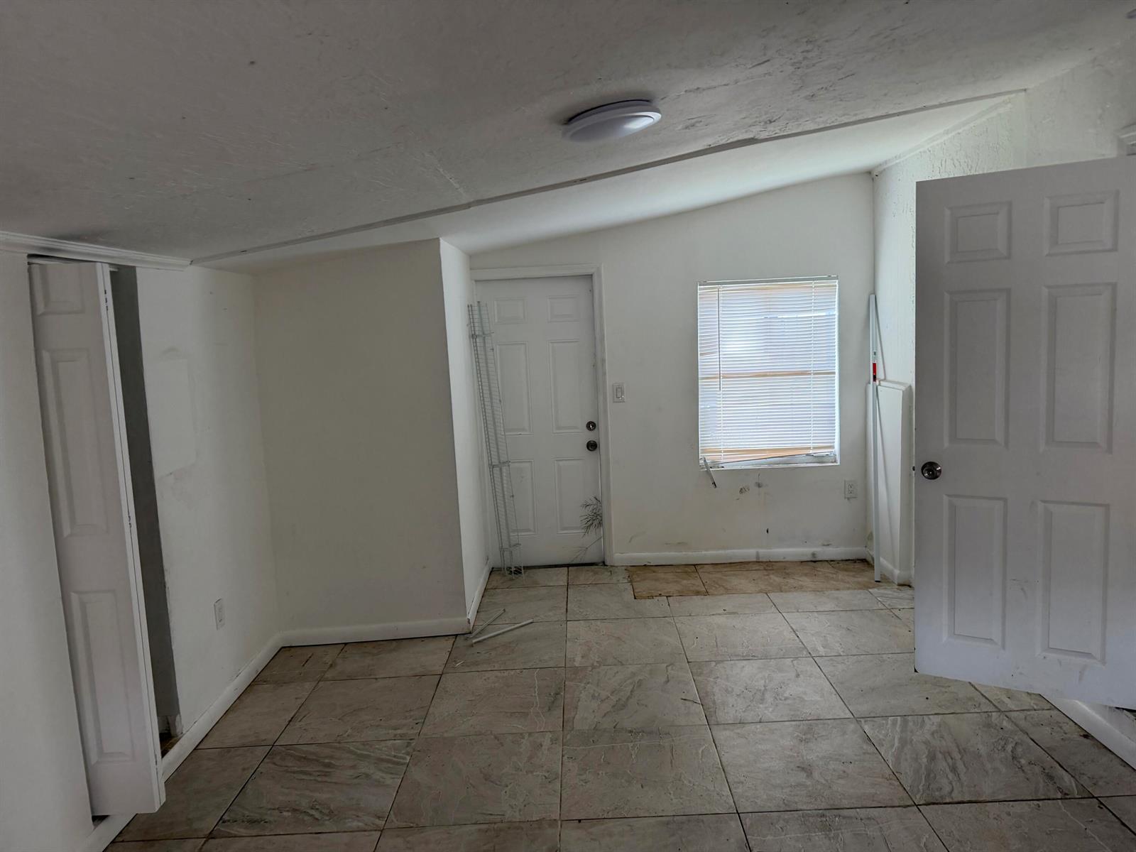 An empty room features white walls, a sloped ceiling, tiled flooring, and two white doors — 115 Maple Avenue, Fort Pierce FL 34982, FORT PIERCE, FL